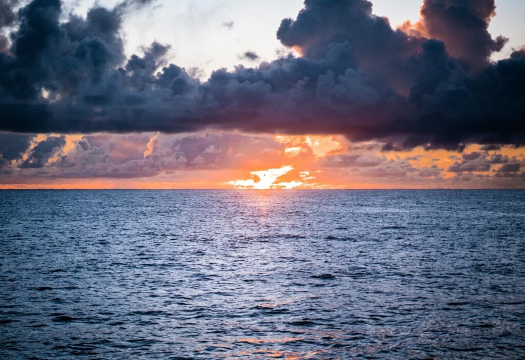 Sunset over the ocean with dramatic clouds illuminated in orange and gold light.