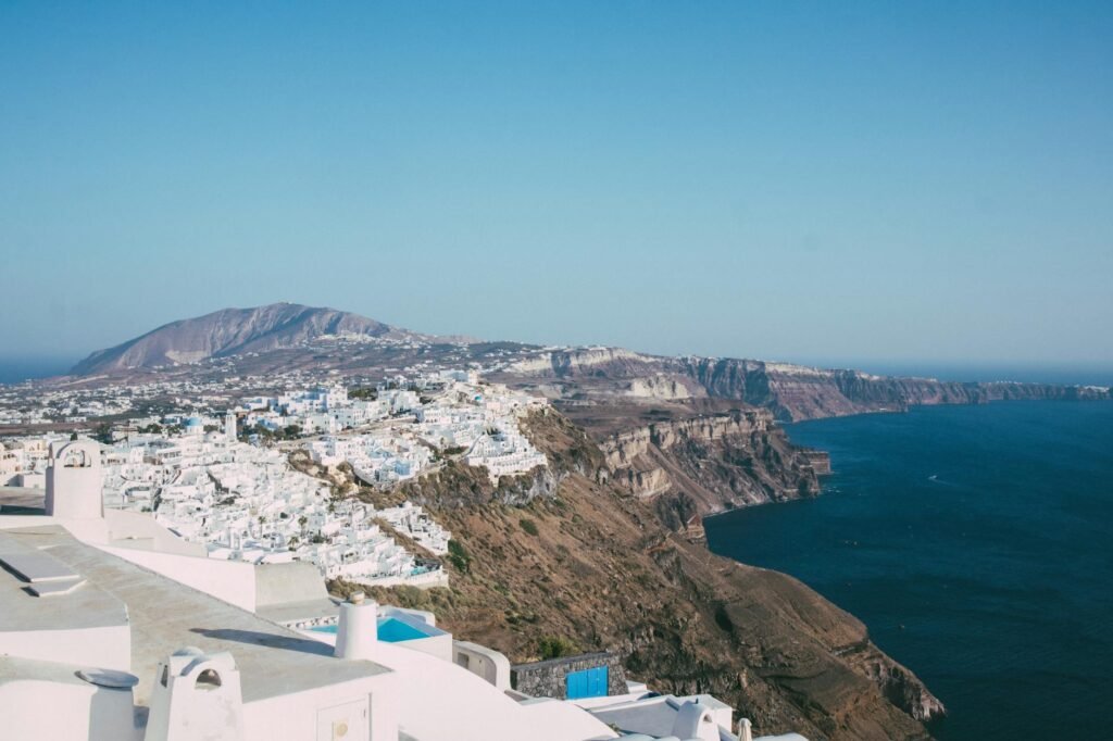 Whitewashed buildings perched on volcanic cliffs above turquoise Aegean Sea waters in Santorini, Greece.