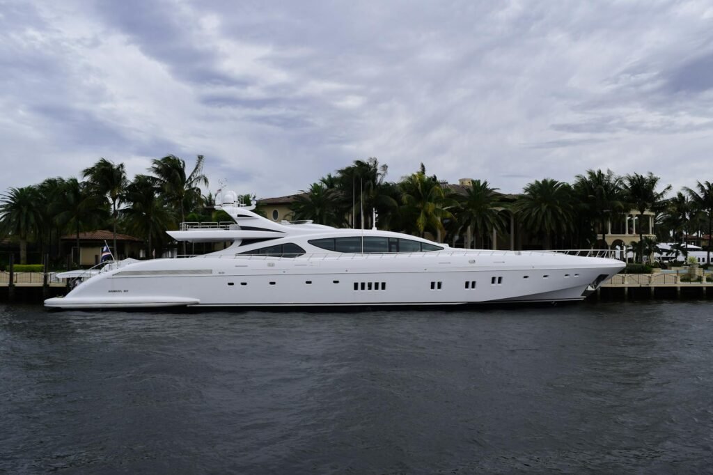 Luxury white yacht moored at Fort Lauderdale waterfront with palm trees and cloudy sky.