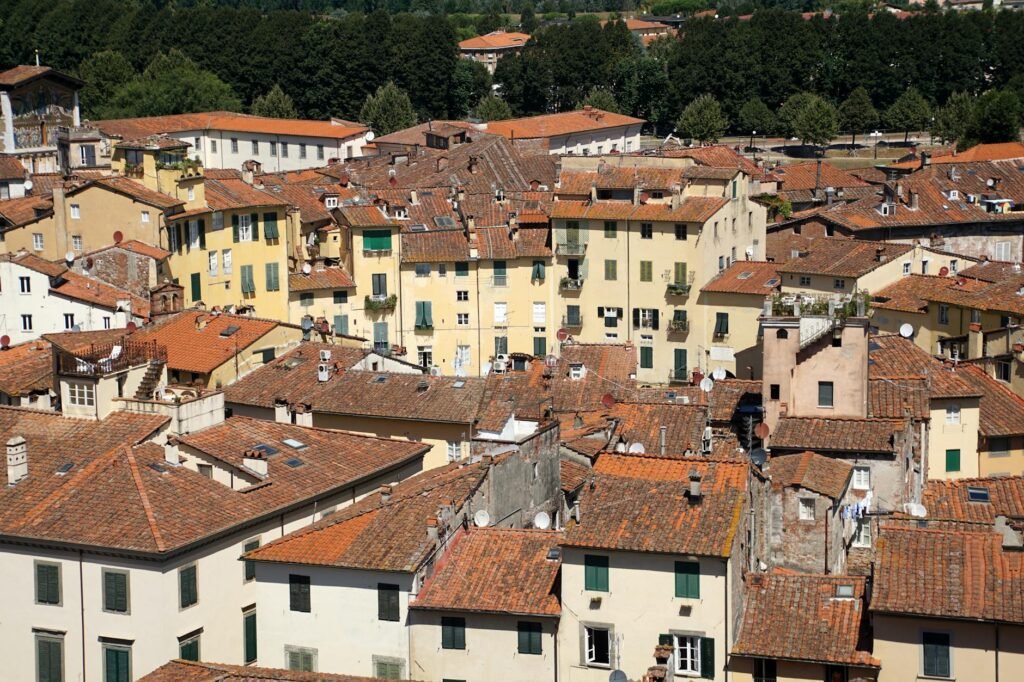 Aerial view of a historic Italian town with terracotta-roofed buildings and yellow facades nestled among green hills.