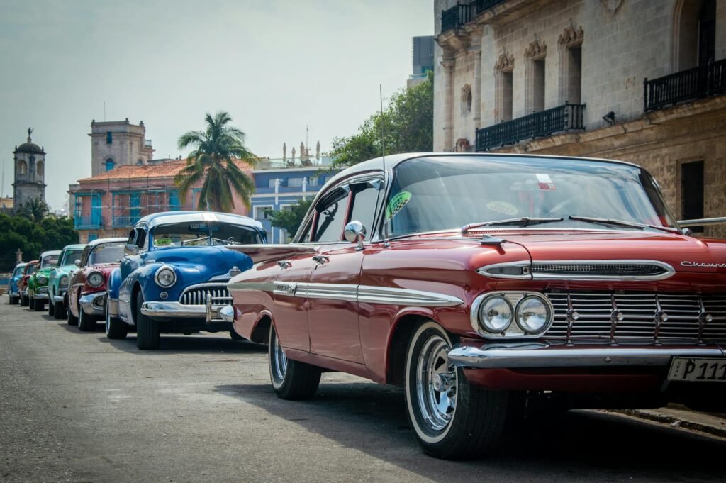 Row of colorful vintage American cars parked in Havana's historic old town square with colonial architecture.