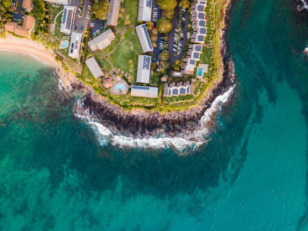 Aerial view of a luxury coastal resort with white buildings, solar panels, and a sandy beach overlooking turquoise ocean…