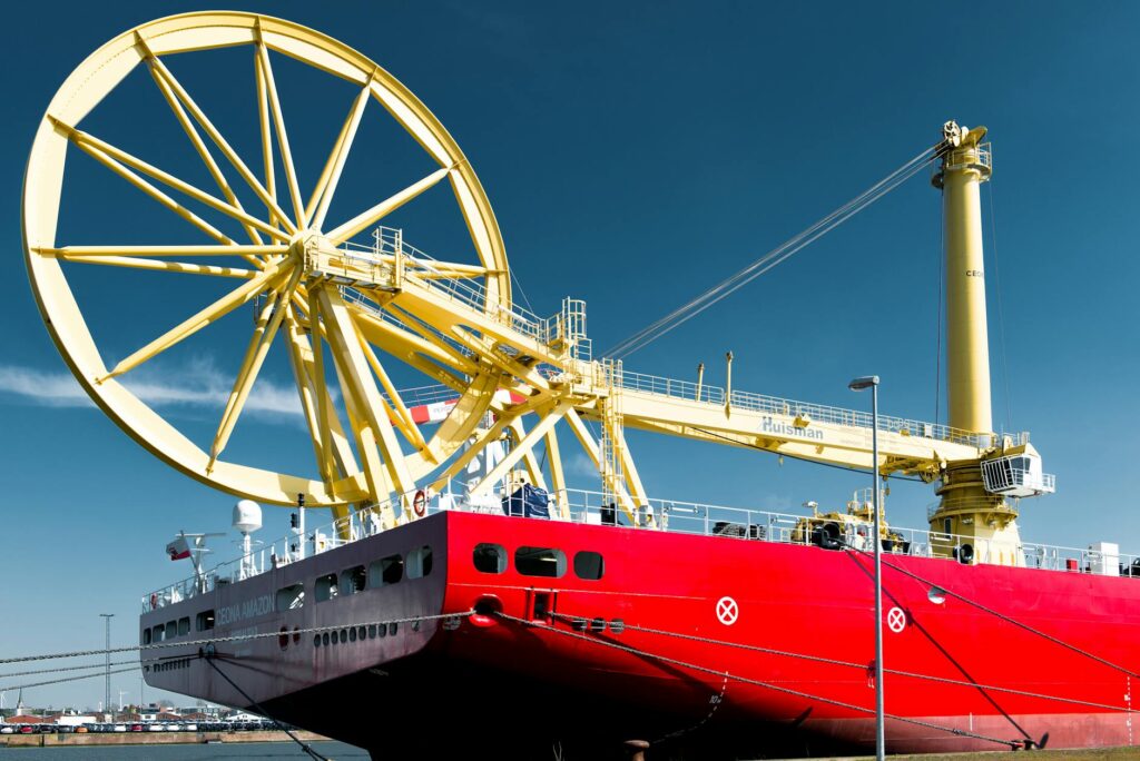 Large red and gray cargo ship with yellow crane and satellite dish docked at Bremerhaven port.