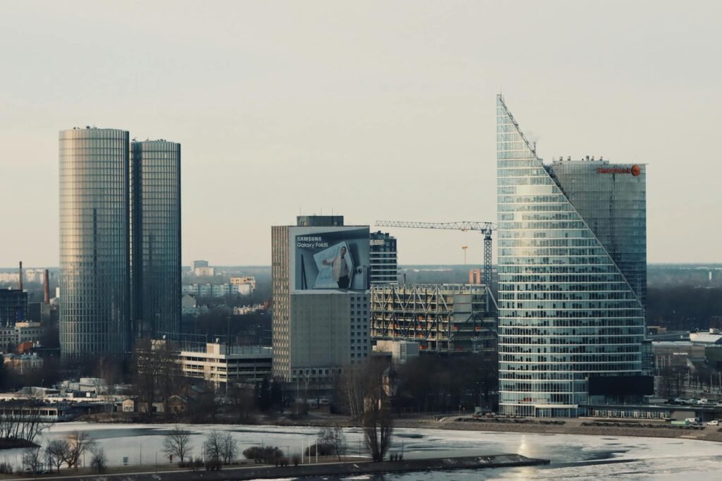 Modern skyscrapers line the Daugava River in Riga's skyline with partially frozen water in foreground.