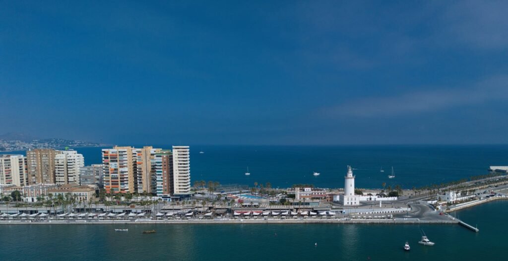 Aerial view of Málaga's coastal waterfront with high-rise beachfront hotels, marina, and lighthouse pier extending into the…