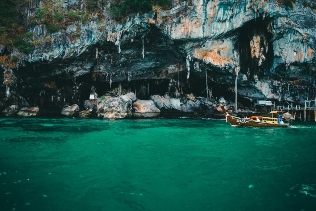 Wooden longtail boat floating in turquoise water near cave entrance and limestone cliffs in Phuket.