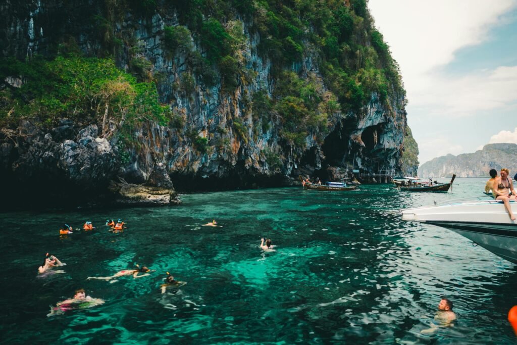 Tourists swimming and snorkeling in crystal-clear turquoise water near towering limestone cliffs in Phuket.