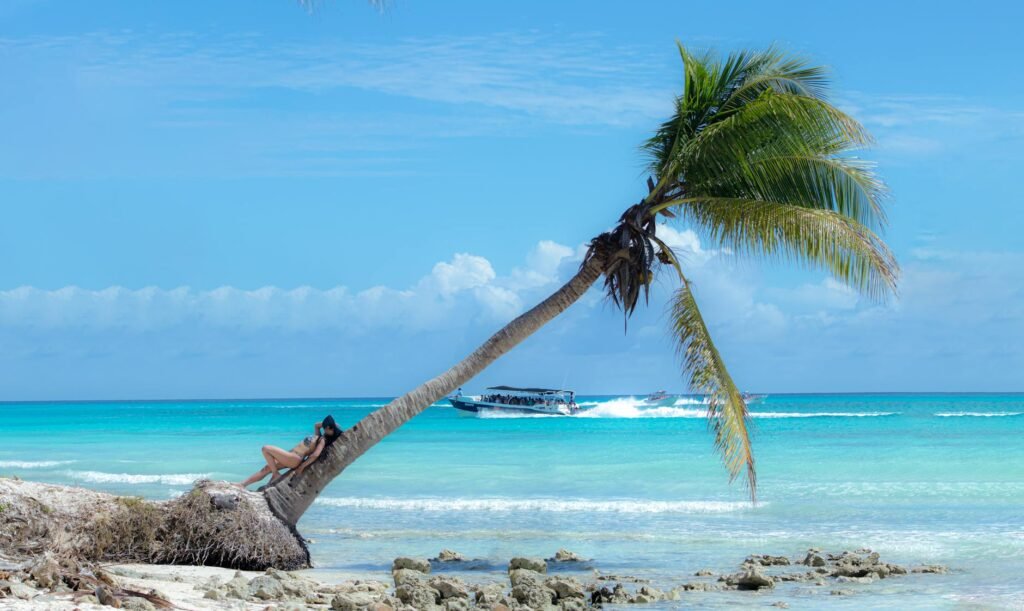 Leaning palm tree on a pristine beach with turquoise waters and a boat offshore.