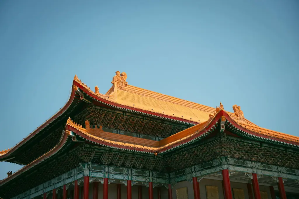 Traditional Chinese temple with golden curved roof and red pillars against clear blue sky.