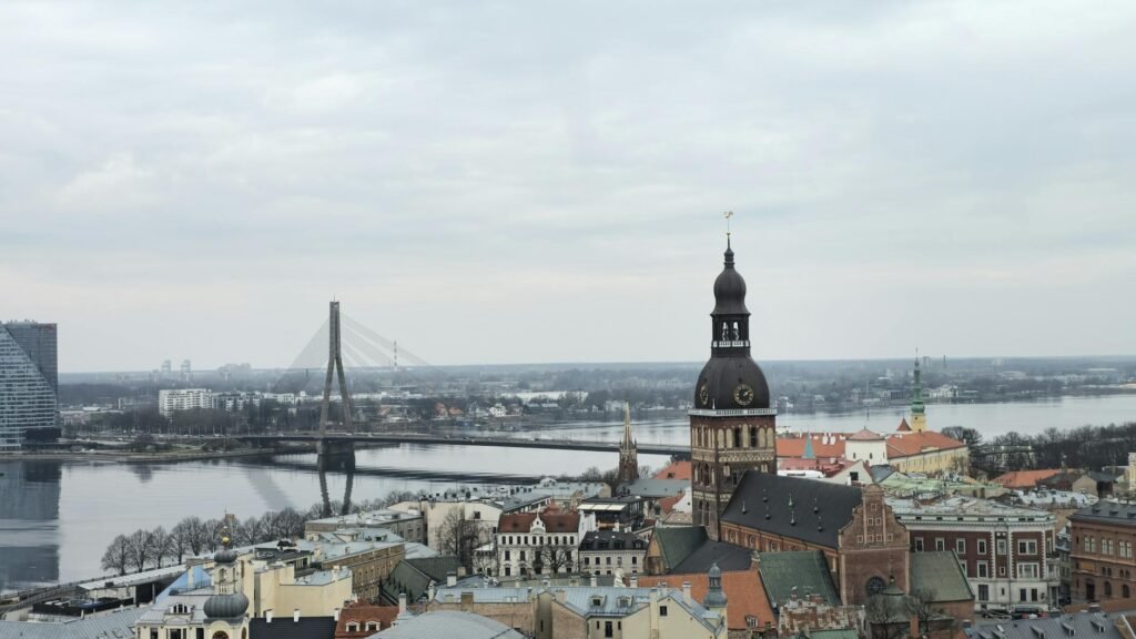 Riga skyline showing Dome Cathedral spire, historic Old Town architecture, and Vansu Bridge spanning the Daugava River.
