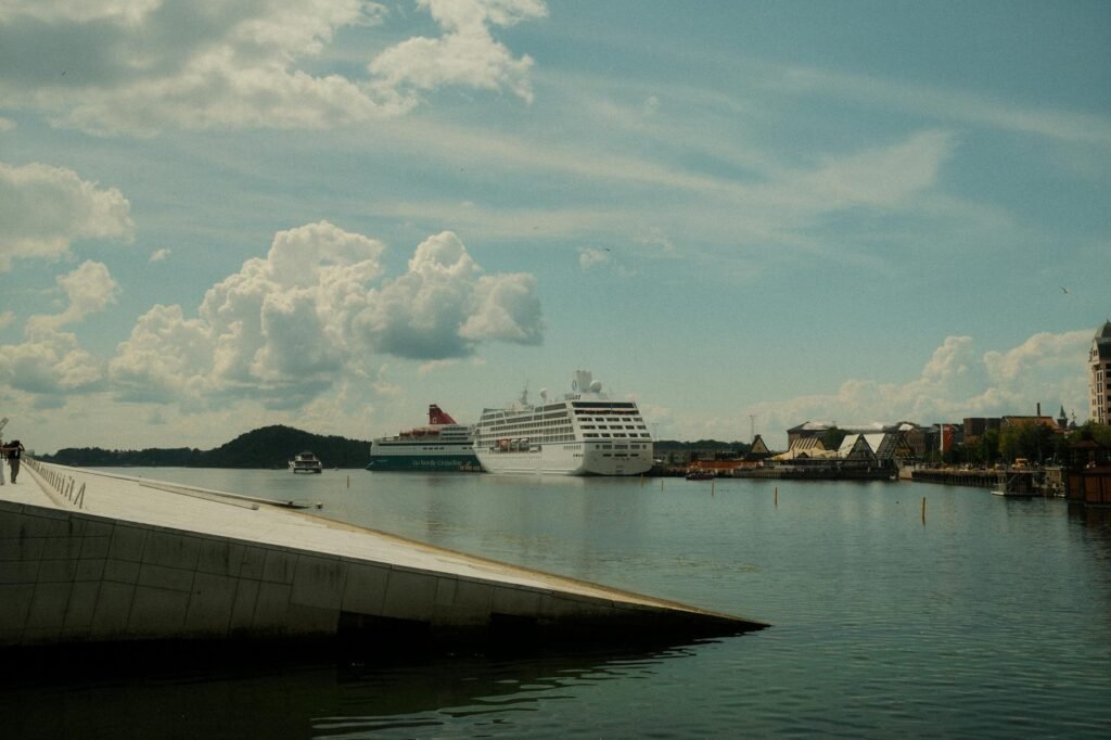Large cruise ship docked in Oslo harbor with waterfront buildings and blue sky with clouds.