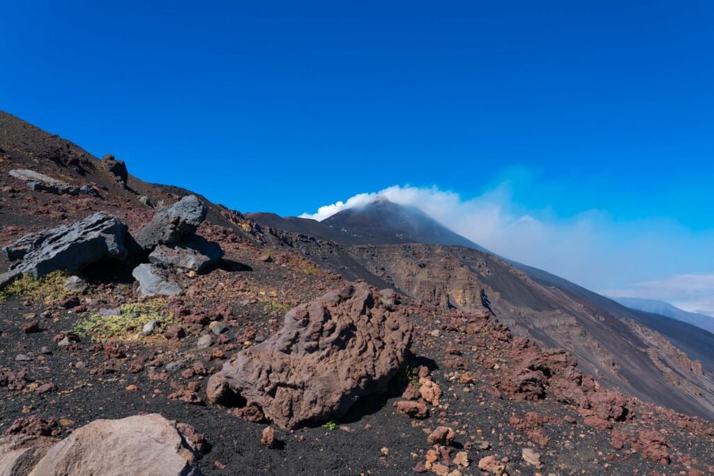 Rocky volcanic slopes of Mount Etna with lava rocks and volcanic cone under clear blue sky.