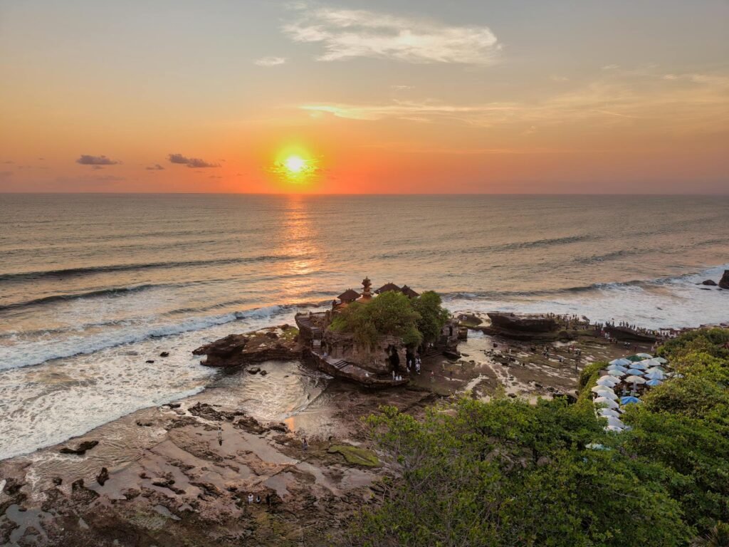 Golden sunset over rocky coastline with ancient temple on island outcrop in Bali waters.