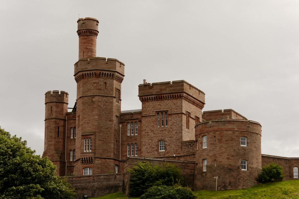 Red sandstone castle with multiple towers and crenellated walls surrounded by green vegetation.