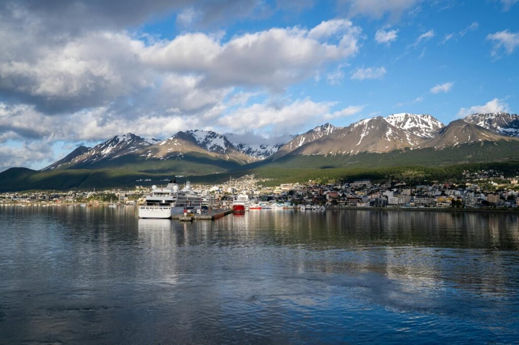 Cruise ship docked in Ushuaia harbor with snow-capped Martial Mountains and coastal town buildings visible.