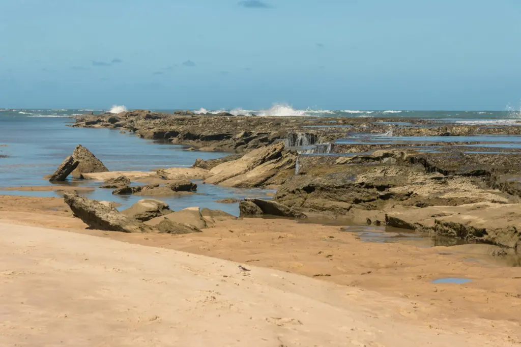 Rocky coastline with sandy beach and tidal pools under blue sky in South Africa.