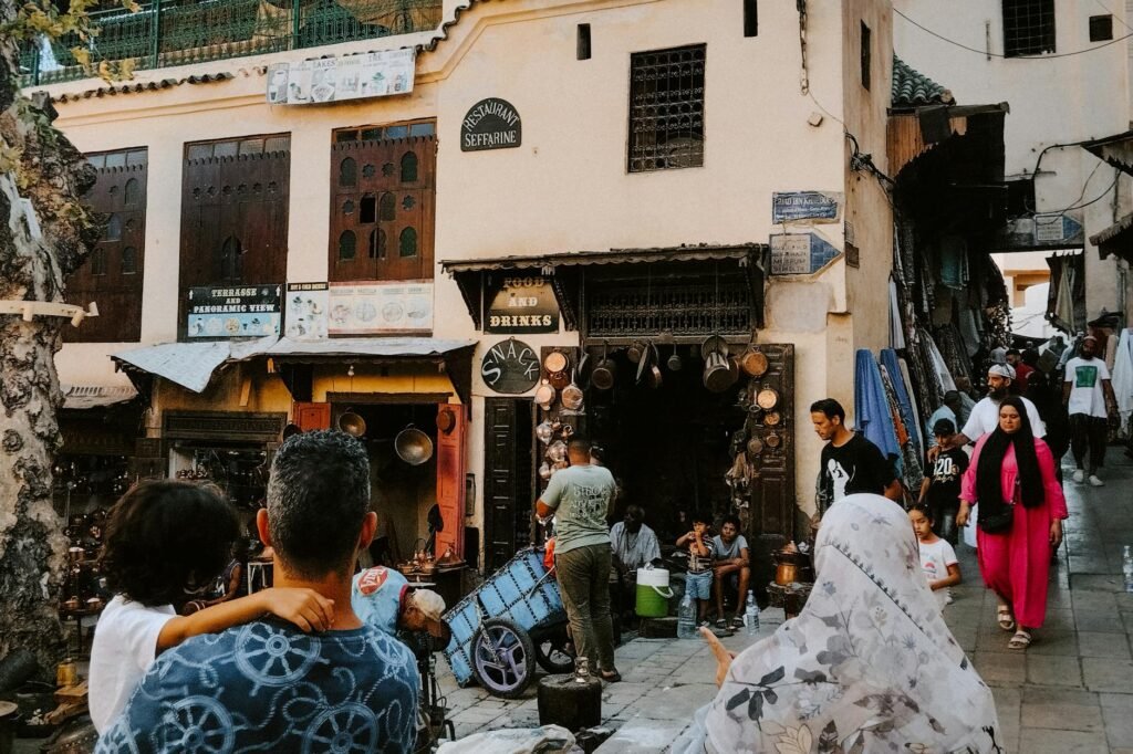 Bustling souk street in Tangier's medina with traditional shops selling crafts and souvenirs, tourists browsing goods…
