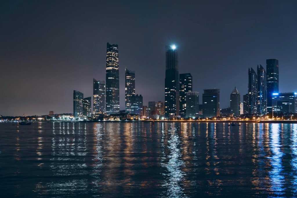 Abu Dhabi skyline at night with illuminated skyscrapers reflecting in calm blue water.
