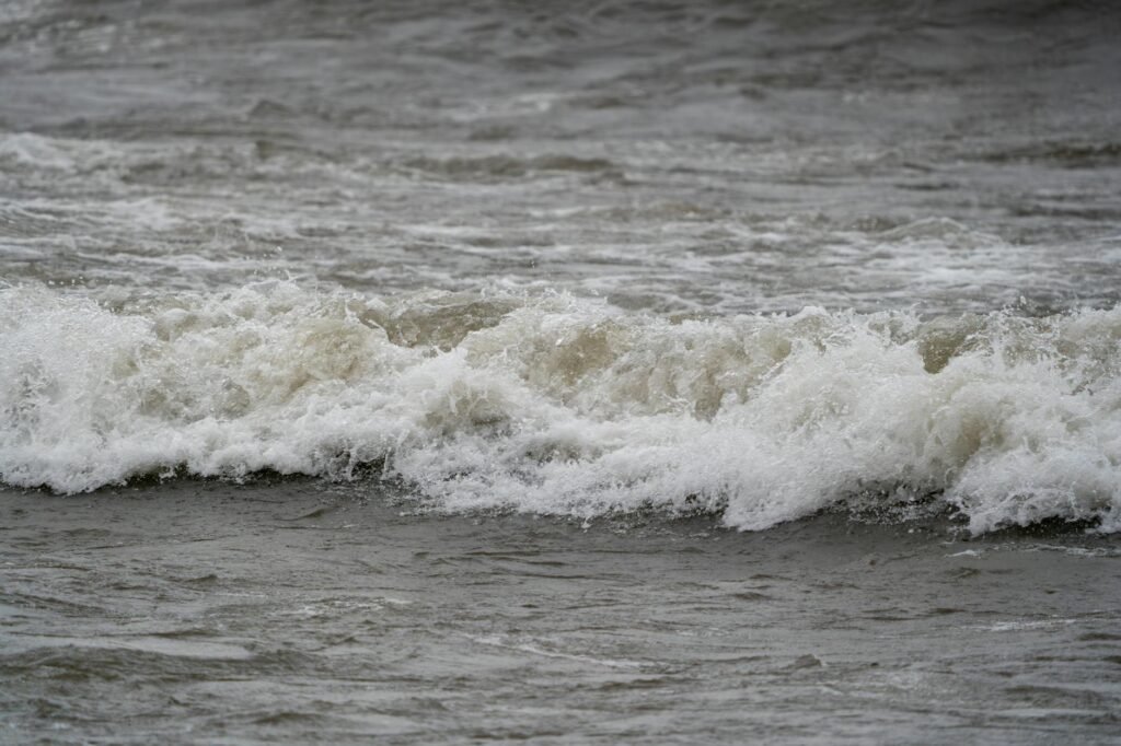 Foamy white waves crash onto a sandy beach with turbulent ocean water in the background.