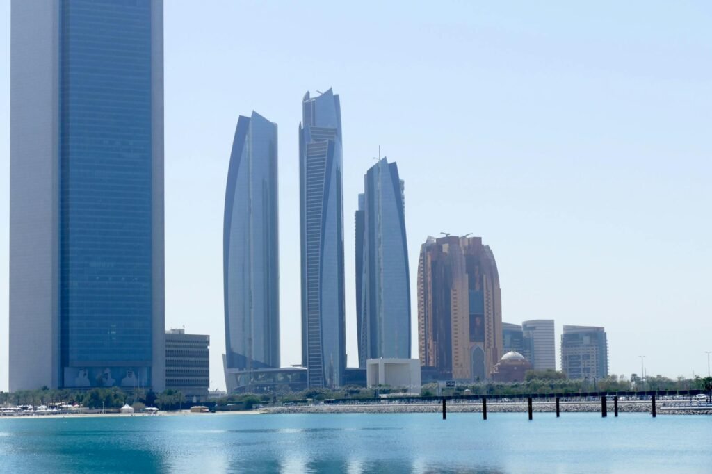 Modern high-rise skyscrapers line the waterfront of Abu Dhabi with turquoise water in the foreground.