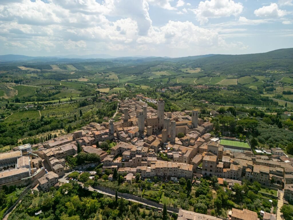 Aerial view of San Gimignano's medieval hilltop town with terracotta rooftops and towers surrounded by Tuscany's green…
