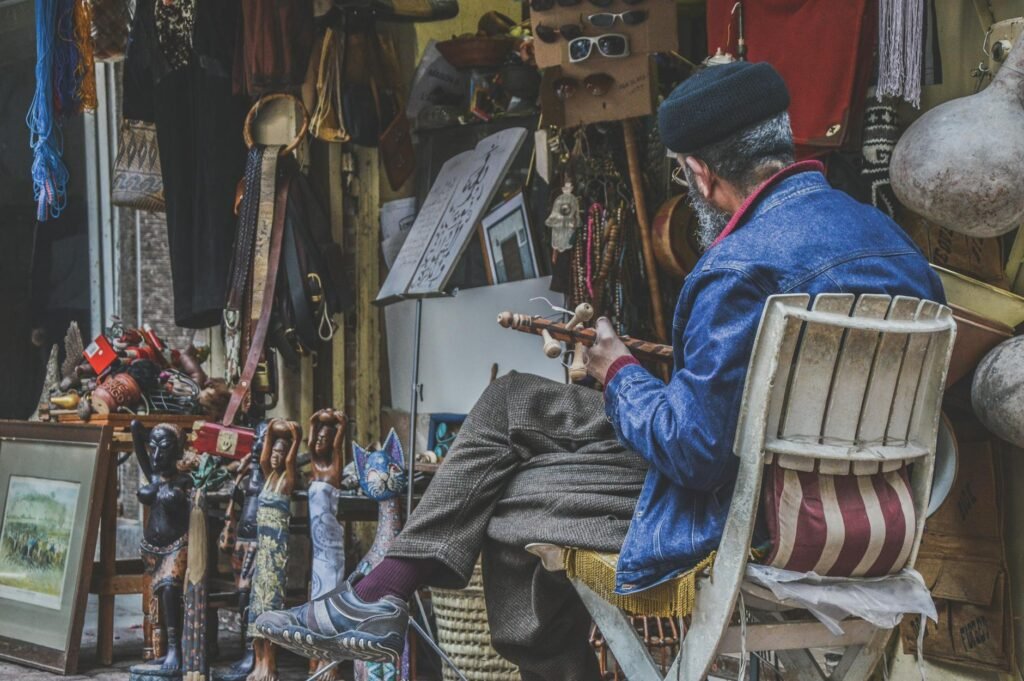 Craftsman in blue jacket working with tools in crowded workshop filled with traditional Moroccan goods and souvenirs.